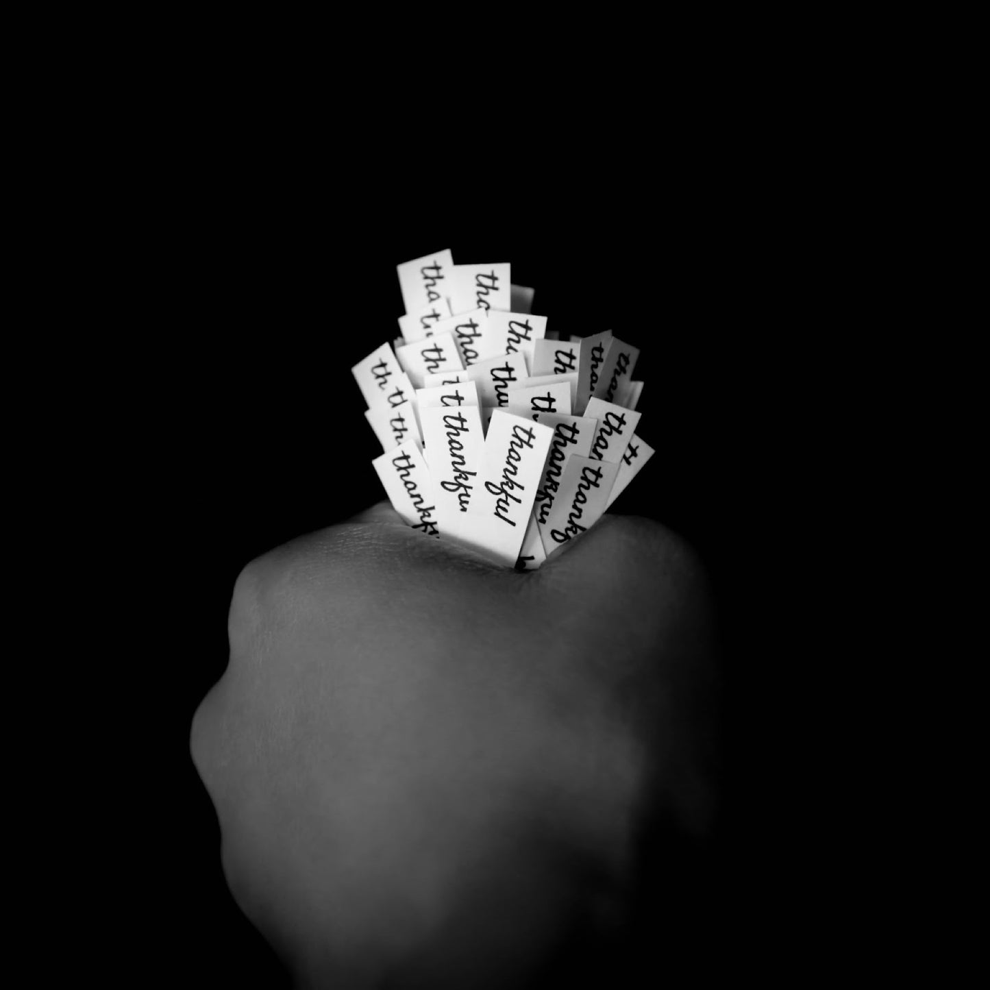 Black and white image of a hand holding a cluster of slips of paper that each read read thankful in a cursive font