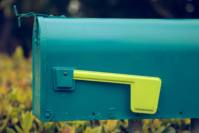 Bright teal mailbox with a neon green flag that is down, photographed from the side