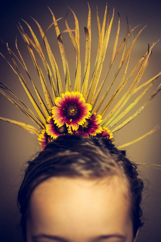 Closeup of a person's head from the eyebrows up wearing a yellow palm frond and pink and yellow flower headpiece