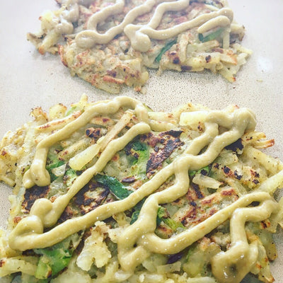 Vegetable pancakes consisting of grated zucchini and potatoes with a yellow sauce zigzag on top