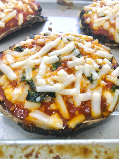Portobello cap mushroom pizzas with vegan cheese, red sauce, and basil on a baking sheet
