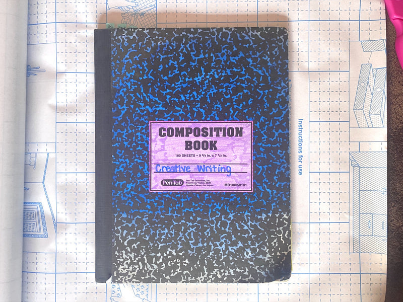 DIY customized composition book colored blue with purple in the center and the label Creative Writing written in blue on the reverse side grid of contact paper